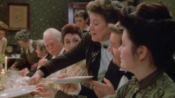 Movie still from “The Dead” (1987), directed by John Huston – A group of people sitting around a table with plates; Medium shot, Over the shoulder angle