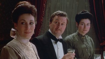 Movie still from “The Dead” (1987), directed by John Huston – A man and two women in formal attire holding a glass of wine; Close Up shot, Over the shoulder angle
