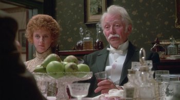 Movie still from “The Dead” (1987), directed by John Huston – An older man sitting at a dinner table with a glass of wine; Medium shot, Over the shoulder angle