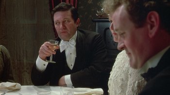 Movie still from “The Dead” (1987), directed by John Huston – A man sitting at a table with a glass of wine in front of him; Close Up shot, Over the shoulder angle