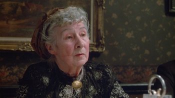 Movie still from “The Dead” (1987), directed by John Huston – An older woman wearing a black dress and a white hat; Close Up shot, High angle