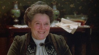 Movie still from “The Dead” (1987), directed by John Huston – An older woman smiling for the camera in front of a table; Close Up shot, Over the shoulder angle