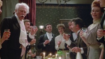 Movie still from “The Dead” (1987), directed by John Huston – A group of people standing in front of a table with food; Medium shot, Low angle