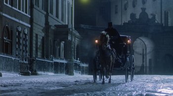 Movie still from “The Dead” (1987), directed by John Huston – A man riding a horse drawn carriage down a street at night; Wide shot, High angle