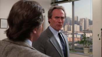 Movie still from “The Dead Pool” (1988), directed by Buddy Van Horn – A man in a suit and tie standing next to another man in front of a window; Close Up shot, Over the shoulder angle