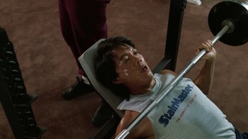 Movie still from “The Dead Pool” (1988), directed by Buddy Van Horn – A young man is sitting on a bench press; Medium shot, Overhead angle