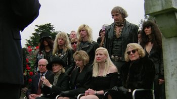 Movie still from “The Dead Pool” (1988), directed by Buddy Van Horn – A group of people sitting in a row wearing all black; Wide shot, High angle