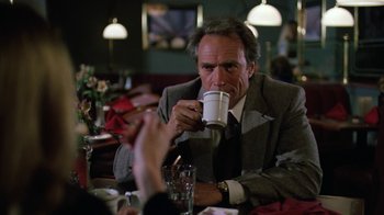 Movie still from “The Dead Pool” (1988), directed by Buddy Van Horn – A man in a suit drinking from a white cup; Medium shot, Over the shoulder angle