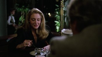 Movie still from “The Dead Pool” (1988), directed by Buddy Van Horn – A woman sitting at a table with a cup of coffee; Medium shot, Over the shoulder angle
