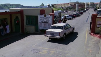 Movie still from “The Dead Pool” (1988), directed by Buddy Van Horn – A white car driving down a street next to a building; Extreme Wide shot, High angle