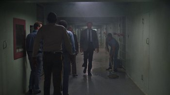 Movie still from “The Dead Pool” (1988), directed by Buddy Van Horn – A group of people in a hallway with a man in a suit and tie; Wide shot, High angle