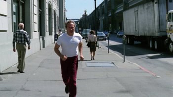 Movie still from “The Dead Pool” (1988), directed by Buddy Van Horn – A man running down the street while wearing headphones; Wide shot, Low angle