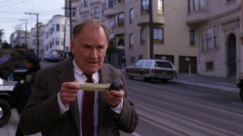 Movie still from “The Dead Pool” (1988), directed by Buddy Van Horn – An older man holding a piece of wood while holding a cell phone; Close Up shot, High angle