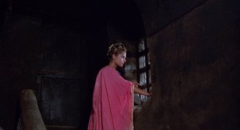 Movie still from “The Decameron” (1971), directed by Pier Paolo Pasolini – A young girl in a pink dress standing next to a window; Medium shot, Low angle