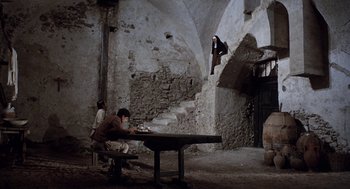 Movie still from “The Decameron” (1971), directed by Pier Paolo Pasolini – A man sitting at a table in a room with stairs; Wide shot, Low angle