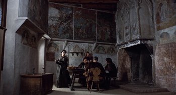 Movie still from “The Decameron” (1971), directed by Pier Paolo Pasolini – A group of people sitting around a table in a room; Wide shot, High angle