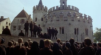 Movie still from “The Decameron” (1971), directed by Pier Paolo Pasolini – A group of people standing in front of a castle; Extreme Wide shot, Low angle