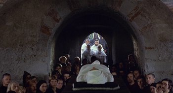 Movie still from “The Decameron” (1971), directed by Pier Paolo Pasolini – A group of people sitting around a body in a tunnel; Wide shot, High angle