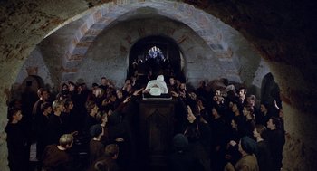 Movie still from “The Decameron” (1971), directed by Pier Paolo Pasolini – A group of people gathered around a statue of jesus; Wide shot, High angle
