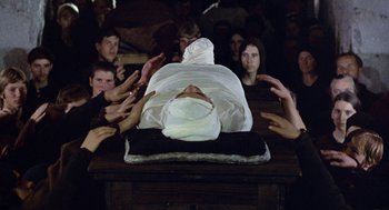 Movie still from “The Decameron” (1971), directed by Pier Paolo Pasolini – A group of people sitting around a person laying on the ground; Medium shot, High angle