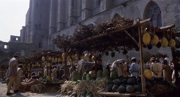Movie still from “The Decameron” (1971), directed by Pier Paolo Pasolini – A group of people standing under a fruit stand; Extreme Wide shot, High angle