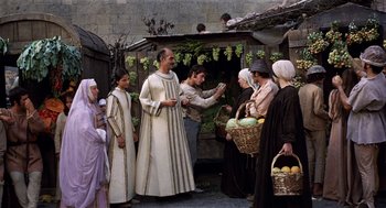 Movie still from “The Decameron” (1971), directed by Pier Paolo Pasolini – A group of people standing next to each other near a building; Wide shot, Over the shoulder angle