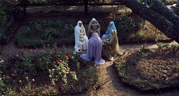 Movie still from “The Decameron” (1971), directed by Pier Paolo Pasolini – A group of people sitting on the ground next to a flower garden; Extreme Wide shot, High angle