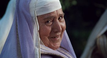 Movie still from “The Decameron” (1971), directed by Pier Paolo Pasolini – An older woman wearing a head covering and smiling for the camera; Close Up shot, Low angle