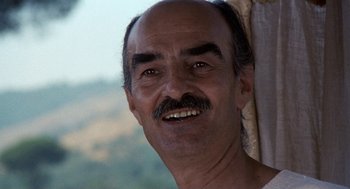 Movie still from “The Decameron” (1971), directed by Pier Paolo Pasolini – An older man with a mustache smiling for the camera; Close Up shot, Low angle