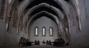 Movie still from “The Decameron” (1971), directed by Pier Paolo Pasolini – A group of people sitting around a table in a room; Extreme Wide shot, High angle