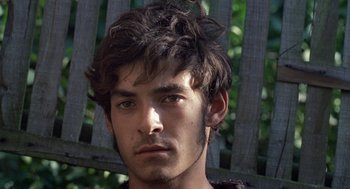 Movie still from “The Decameron” (1971), directed by Pier Paolo Pasolini – A young man with brown hair and green eyes stares into the camera; Close Up shot, High angle