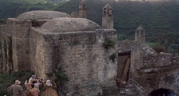 Movie still from “The Decameron” (1971), directed by Pier Paolo Pasolini – An image of an old building with a woman standing on the side of it; Extreme Wide shot, Low angle