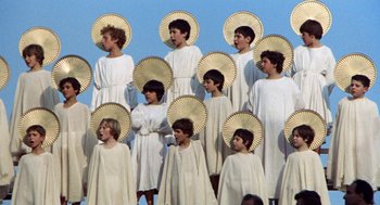 Movie still from “The Decameron” (1971), directed by Pier Paolo Pasolini – A group of young people dressed in white and holding parasols; Wide shot, Overhead angle