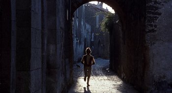 Movie still from “The Decameron” (1971), directed by Pier Paolo Pasolini – A person walking down a street in the sunlight; Wide shot, Over the shoulder angle
