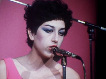 Movie still from “The Decline of Western Civilization” (1981), directed by Penelope Spheeris – A person holding a microphone on a microphone stand; Close Up shot, Low angle