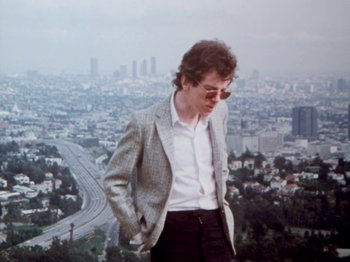 Movie still from “The Decline of Western Civilization” (1981), directed by Penelope Spheeris – A man standing on top of a hill in front of a city; Medium shot, High angle