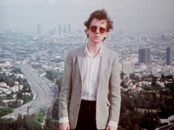 Movie still from “The Decline of Western Civilization” (1981), directed by Penelope Spheeris – A man standing in front of a city skyline; Medium shot, Low angle