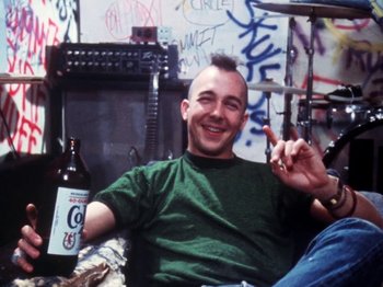 Movie still from “The Decline of Western Civilization” (1981), directed by Penelope Spheeris – A man sitting in a room with a bottle of beer; Medium shot, Low angle