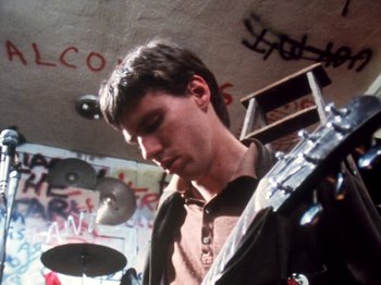 Movie still from “The Decline of Western Civilization” (1981), directed by Penelope Spheeris – A man with a guitar in a room with graffiti on the walls; Medium shot, Low angle