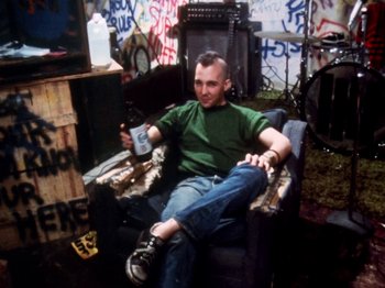 Movie still from “The Decline of Western Civilization” (1981), directed by Penelope Spheeris – A man sitting in a chair holding a bottle; Medium shot, High angle