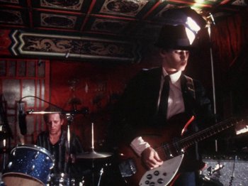 Movie still from “The Decline of Western Civilization” (1981), directed by Penelope Spheeris – A man in a suit and hat playing a guitar; Medium shot, Low angle