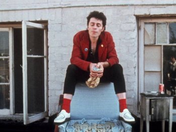 Movie still from “The Decline of Western Civilization” (1981), directed by Penelope Spheeris – A man sitting on a chair holding a can of soda; Medium shot, Low angle