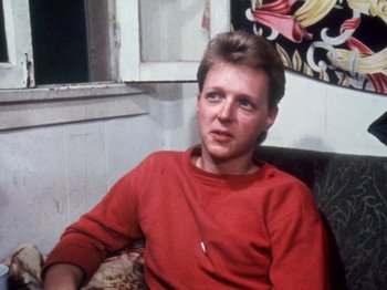Movie still from “The Decline of Western Civilization” (1981), directed by Penelope Spheeris – A man sitting on a couch wearing a red shirt; Close Up shot, Over the shoulder angle