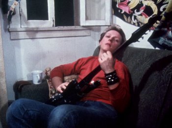 Movie still from “The Decline of Western Civilization” (1981), directed by Penelope Spheeris – A man sitting in a chair holding a guitar; Medium shot, Low angle