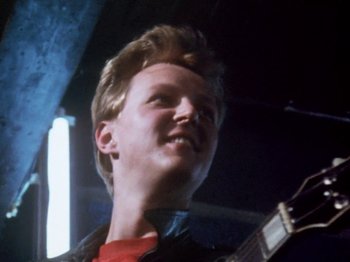 Movie still from “The Decline of Western Civilization” (1981), directed by Penelope Spheeris – A young man holding a guitar in his hands; Close Up shot, Low angle