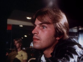 Movie still from “The Decline of Western Civilization” (1981), directed by Penelope Spheeris – A man with long brown hair is looking at the camera; Close Up shot, Low angle