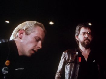 Movie still from “The Decline of Western Civilization” (1981), directed by Penelope Spheeris – Two men standing next to each other in a dark room; Medium shot, Low angle