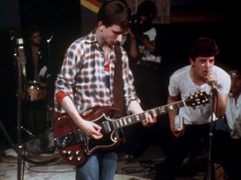 Movie still from “The Decline of Western Civilization” (1981), directed by Penelope Spheeris – Two young men are playing guitar in front of a crowd; Medium shot, Low angle