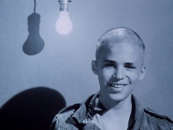 Movie still from “The Decline of Western Civilization” (1981), directed by Penelope Spheeris – A young man with a shaved head smiling for the camera; Close Up shot, High angle