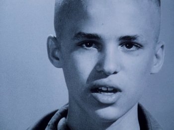 Movie still from “The Decline of Western Civilization” (1981), directed by Penelope Spheeris – A young man with a shaved head is looking at the camera; Close Up shot, High angle